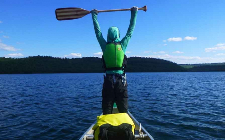 a student stands at the front a canoe and raises their paddle in the air on an outward bound course